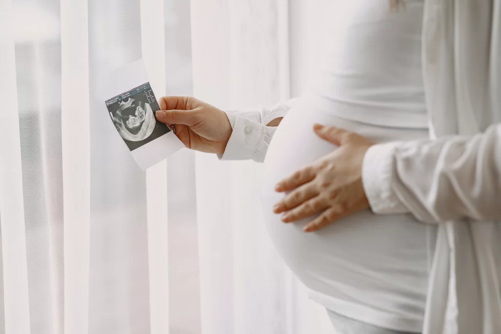 Pregnant-woman-standing-by-window-looking-photo